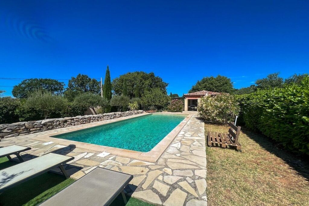Ein rechteckiger Pool mit Steinbord, umgeben von einer Steinterrasse und einer Holzterrasse mit Liegestühlen.