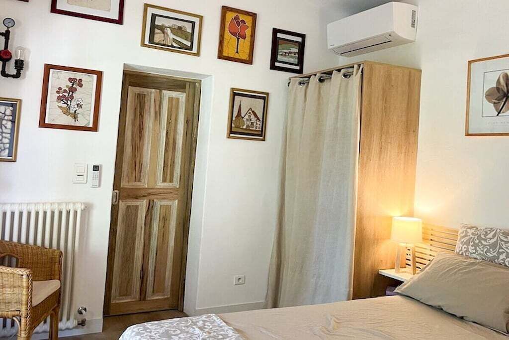 A bedroom with a bed, a wooden wardrobe, a radiator, and a wall-mounted air conditioner.