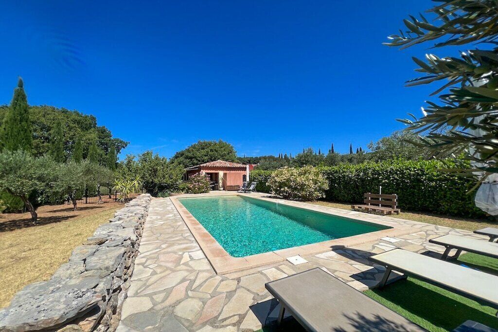 A swimming pool with stone tiles, surrounded by a stone wall and greenery.