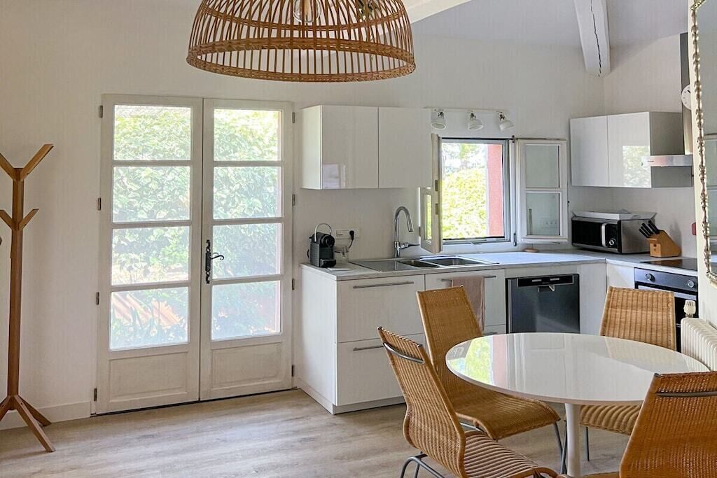 A modern kitchen with white cabinetry, a round dining table, wicker chairs, and a hanging light fixture.