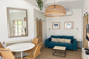 A modern living room with a round dining table, wicker chairs, a blue sofa, and a hanging light fixture. - Holiday home in Aups with swimming pool (Aups)