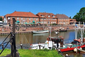 Un pueblo a orillas del río con edificios históricos, un muelle con barcos y una pequeña caseta para botes.