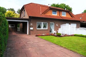 Een tweelaags huis met een rode pannendak, een overdekte oprit en een verzorgd gazon.