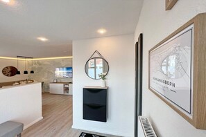 A modern interior with a reception desk, a mounted mirror, a framed map, and a built-in heater. - Holiday apartment Am Stadtwald 319611 (Kühlungsborn)