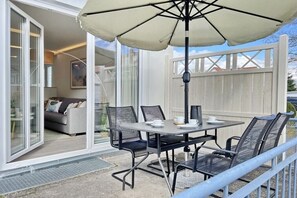 An outdoor patio with a table and chairs, a large umbrella, and a view of the interior through glass doors. - Holiday apartment Am Stadtwald 319611 (Kühlungsborn)