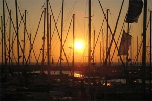 Un port de plaisance où sont amarrés de nombreux bateaux, un ciel dégagé et le soleil qui se couche à l’horizon.
