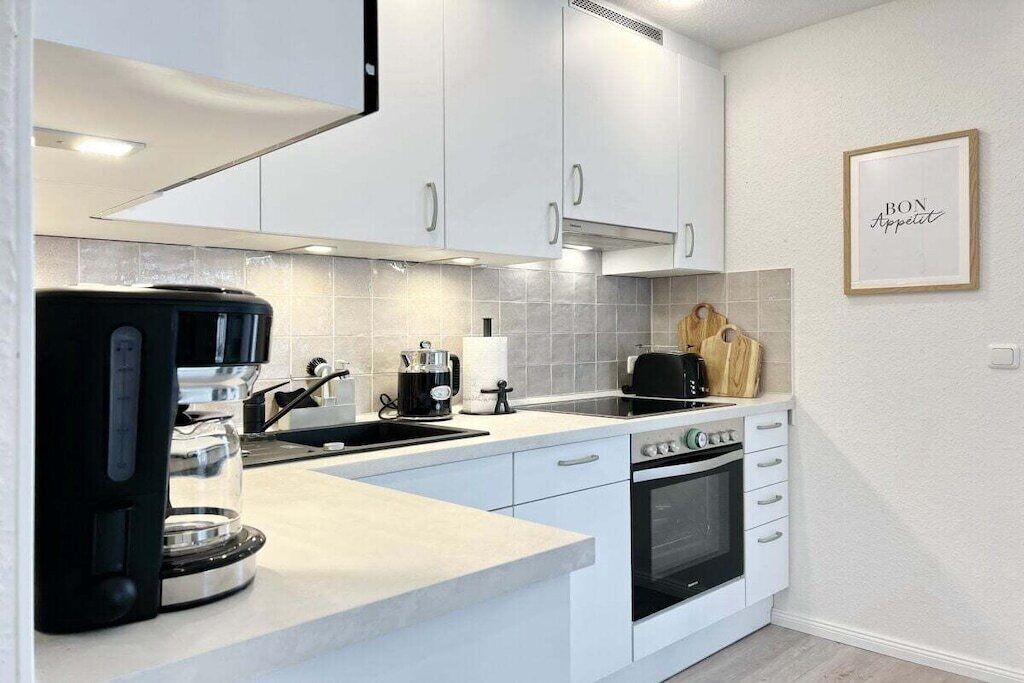 Une cuisine moderne avec des armoires blanches, un four encastré, une machine à café et un panneau décoratif accroché au mur.