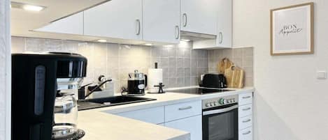 A modern kitchen with white cabinets, a built-in oven, a coffee maker, and a framed sign on the wall.