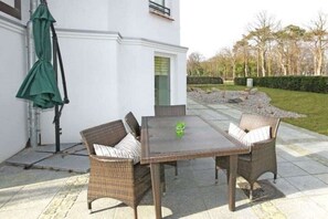 Un patio al aire libre con una mesa, sillas, un paraguas verde y un edificio blanco al fondo.