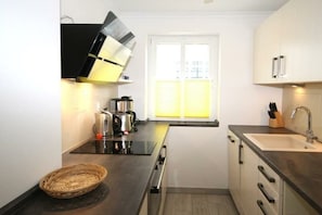 Una cocina moderna con encimera negra, electrodomésticos de acero inoxidable, una ventana con persianas y un lavamanos.