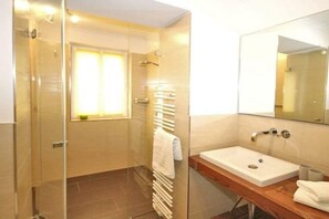 Un baño con cabina de ducha de vidrio, un lavabo blanco y un espejo encima.