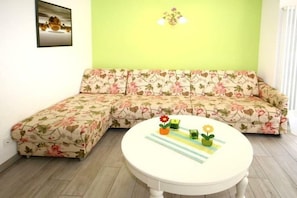 Una habitación con un sofá floral, una mesa redonda con mantel a rayas y una lámpara fijada a la pared.