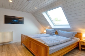 Ein Schlafzimmer mit geneigter Decke, einem Oberlicht, einem Bett mit Holzrahmen, einem Nachttisch mit Lampe und einem Heizkörper.