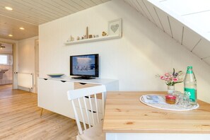 Eine moderne Küche mit einem Holztisch, einem weißen Stuhl, einem Fernseher und einer Regal mit Dekoration.