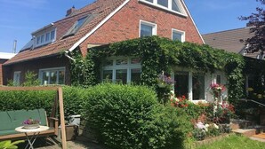 Een tweelaags huis met een schuin dak, een bakstenen gevel en een tuin met diverse planten en bloemen.