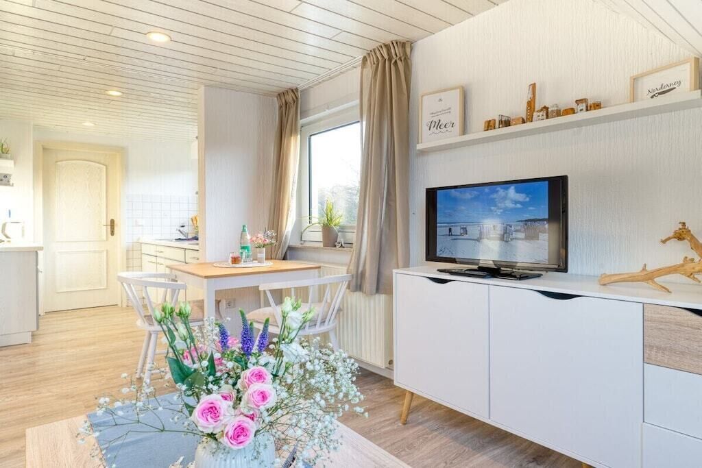 Een moderne woonkamer met een televisie, een eethoek met een tafel en stoelen, en een decoratieve vaas met bloemen.