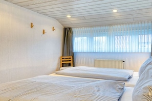 Ein Zimmer mit zwei Betten, einem Sessel, einem Fenster mit Vorhängen und einer Heizung.
