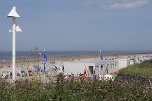 Een strand met een wit gebouw, parasols en mensen.