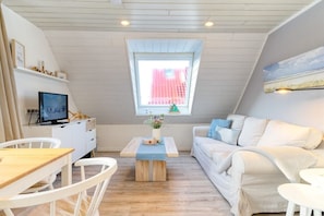 Een gezellige kamer met een witte bank, een houten salontafel, een televisie en een raam met uitzicht op gebouwen.