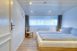 Een slaapkamer met een houten bed, een stoel, een raam met gordijnen en een radiator.