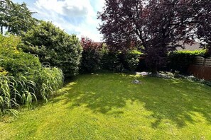 A well-maintained grassy area with a variety of shrubs and trees, a clear sky, and a house in the background. - Holiday home in Rees with swimming pool (Rees)