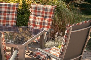 A patio area with a glass-top table and matching chairs, surrounded by greenery. - Holiday home in Rees with swimming pool (Rees)