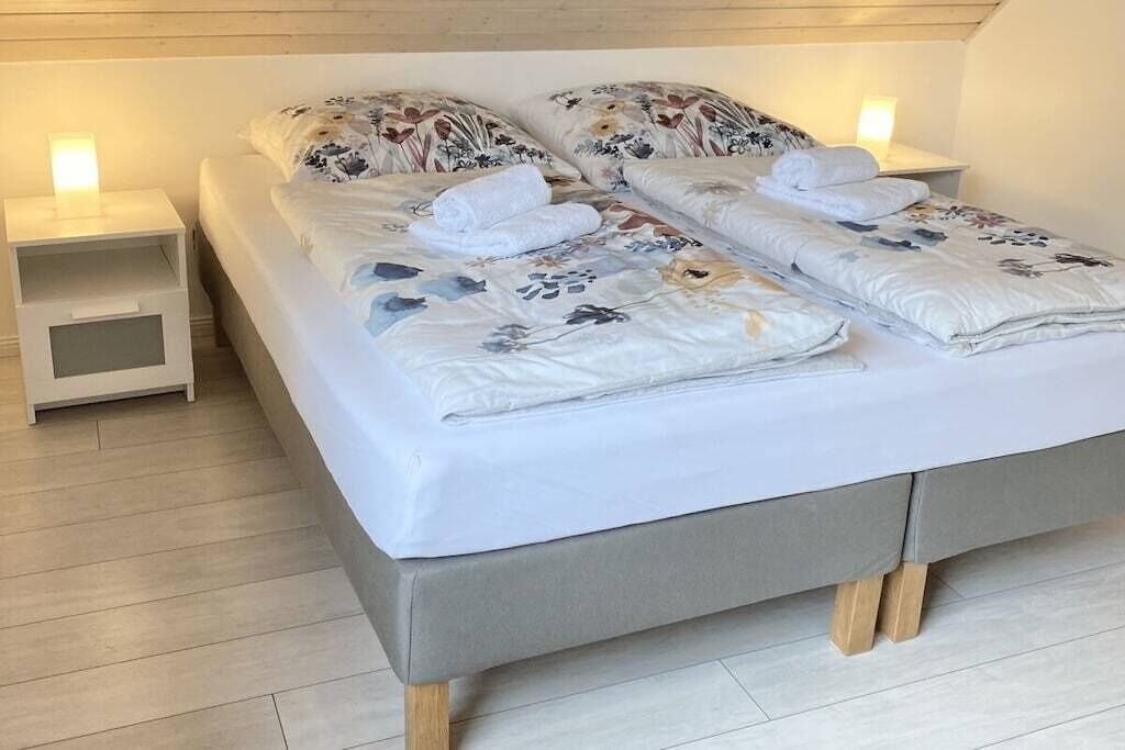 Ein ordentlich bezogenes Bett mit Blumenmuster, zwei Nachttische mit Lampen und ein Holzboden.