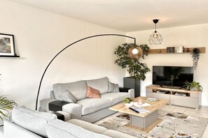 A modern living room with a grey sofa, a coffee table, a TV, and a large plant. - Holiday home in Rees with swimming pool (Rees)