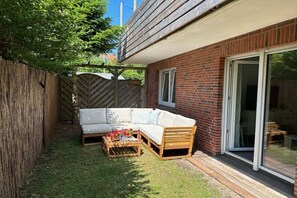Een terras met een houten bank, een bijzettafeltje en een glazen deur naar een kamer.