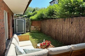 A backyard with a wooden fence, a shed, a lawn, and a seating area with a table and cushions. - Holiday apartment with 2 bedrooms (Norderney)