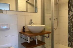 Une salle de bain avec un lavabo blanc, un miroir et un espace douche.