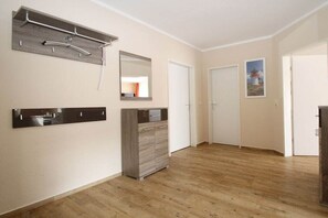 Ein Flur mit Holzboden, einem Kleiderständer, einem Spiegel, einem Schrank und einer Tür.