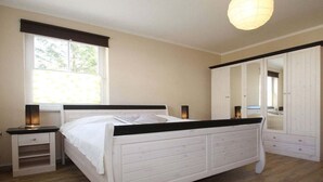 Quarto com cama, mesas de cabeceira, guarda-roupa e janela.