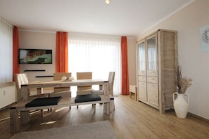 A dining area with a wooden table and chairs, a television mounted on the wall, and a cabinet with drawers. - Holiday apartment Strandstraße 43 319568 (Kühlungsborn-Ost)