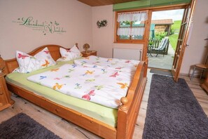 A bedroom with a wooden bed, floral bedding, a view of the garden through a glass door, and a wall decoration. - Holiday apartment with 1 bedroom (Füssen)