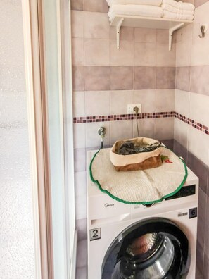 Una sala amb bugaderia que inclou una rentadora, un escorredor i una prestatgeria per a tovalloles.