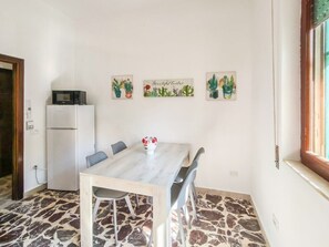 Ein Essbereich mit Tisch, Stühlen, einem Kühlschrank und drei Wanddekorationen mit Kaktusmotiven.