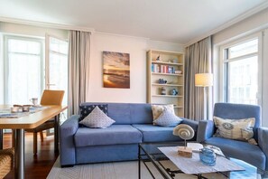 A living room with a sofa, a coffee table, a bookshelf, and a dining area. - 3 (Beach Magic) in Villa Helene (Ostseebad Binz)