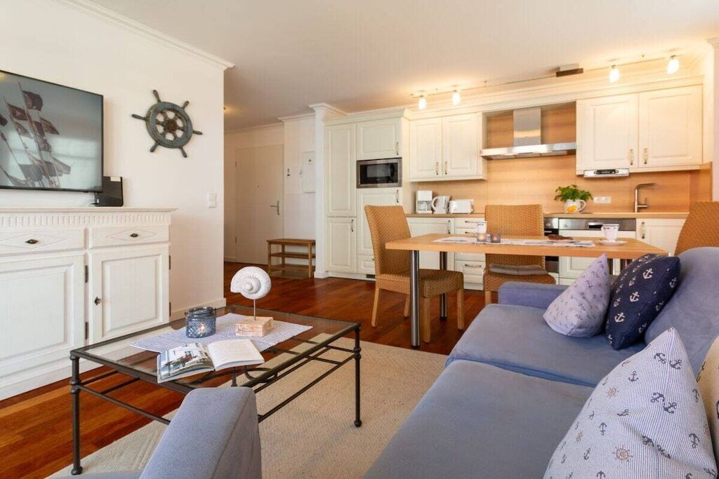 A compact living space with a sofa, a coffee table, a dining table with chairs, a kitchen area with cabinets, and a television.