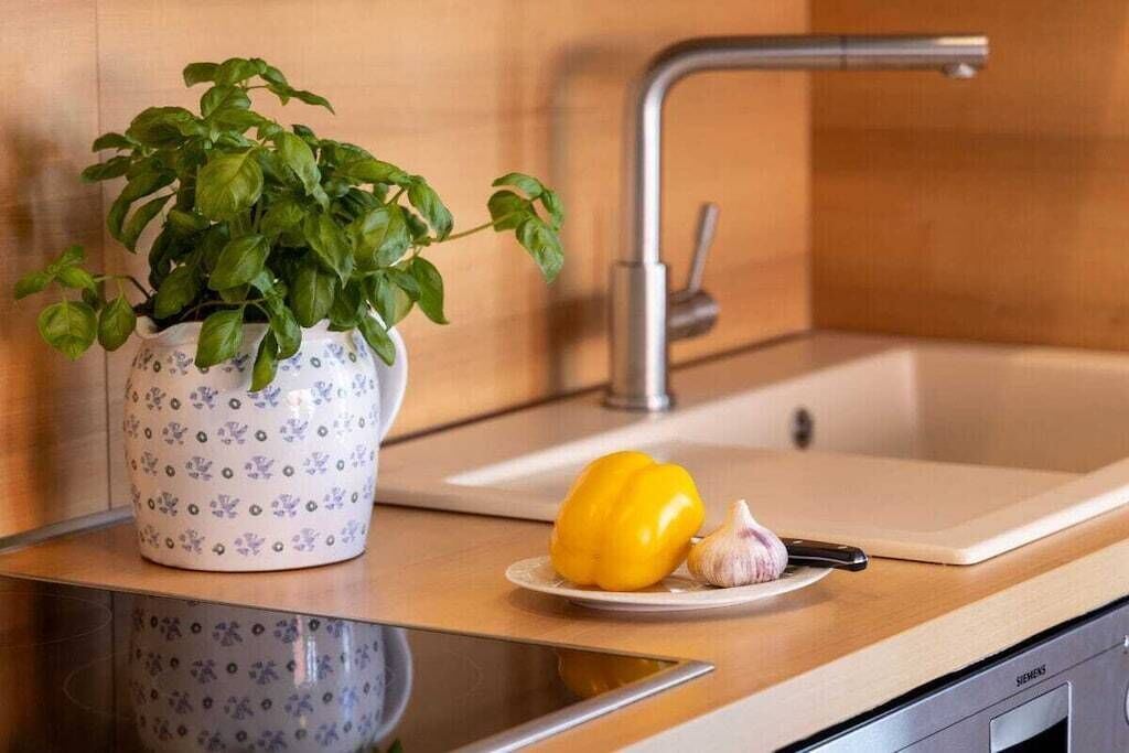 A kitchen counter with a potted basil plant, a yellow bell pepper, and a garlic clove.
