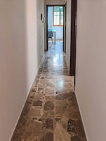 Un pasillo con piso de piedra que lleva a una habitación con ventana y escritorio.