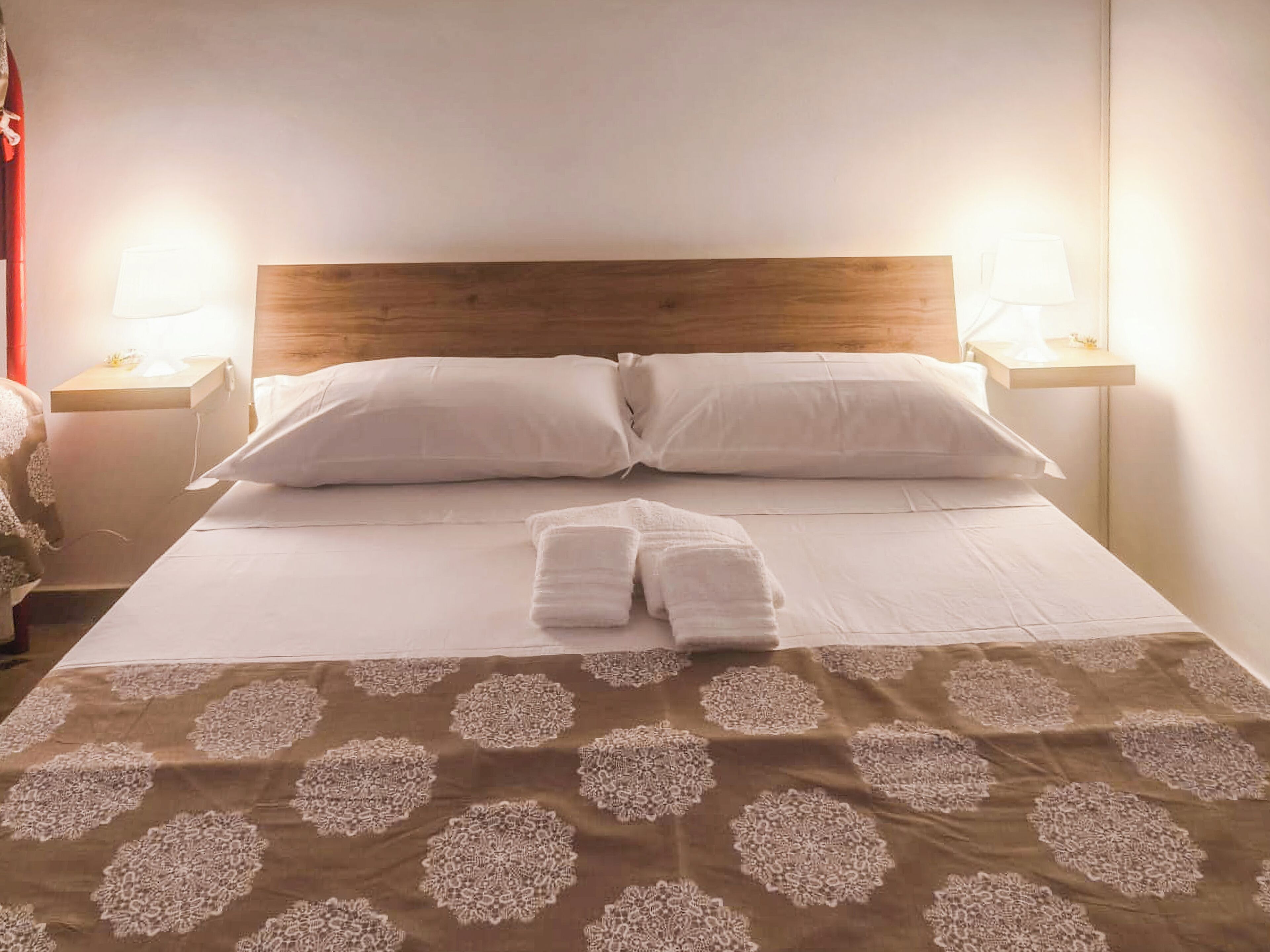 Una cama bien hecha con una colcha marrón estampada, dos almohadas blancas y un par de toallas dobladas.