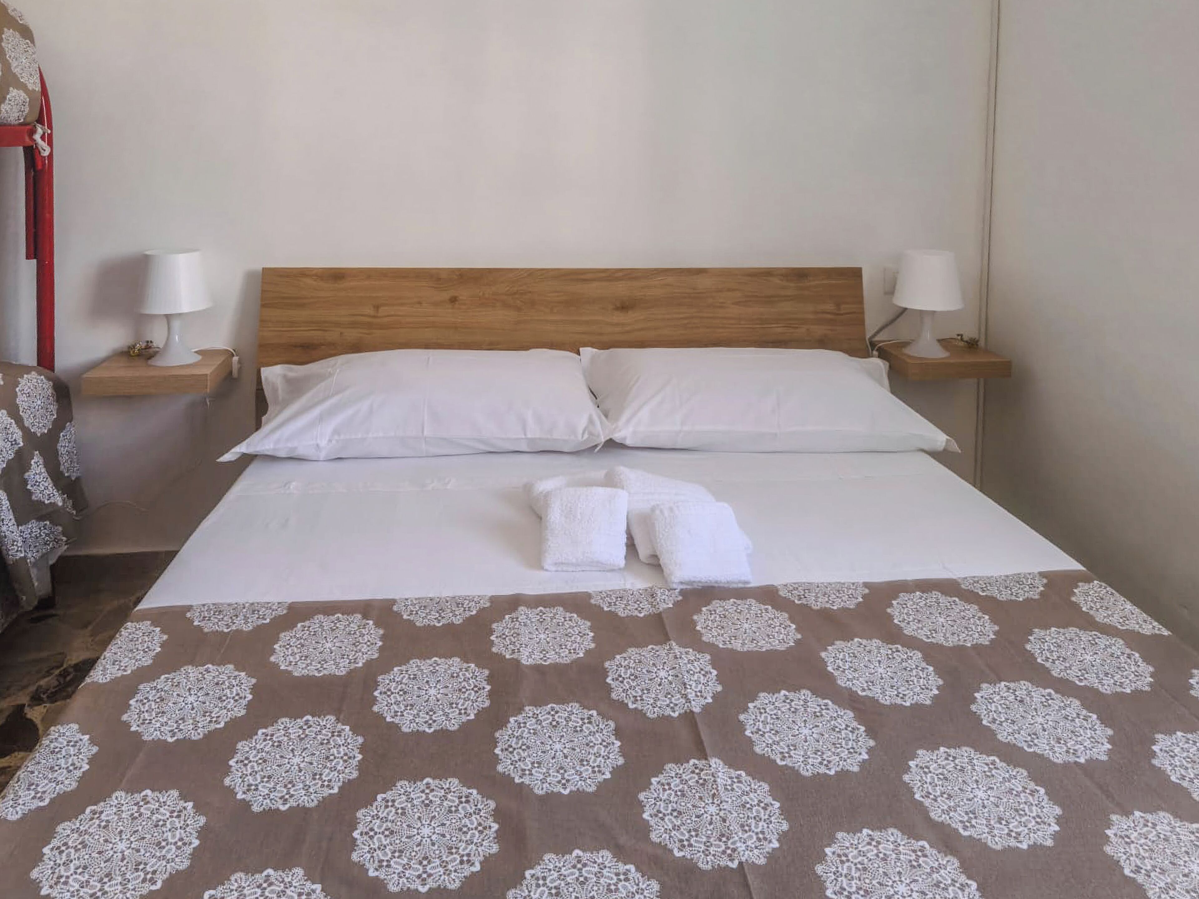 A neatly made bed with white linens, two pillows, and a brown blanket with a white pattern. There are two bedside tables with lamps and a red chair.