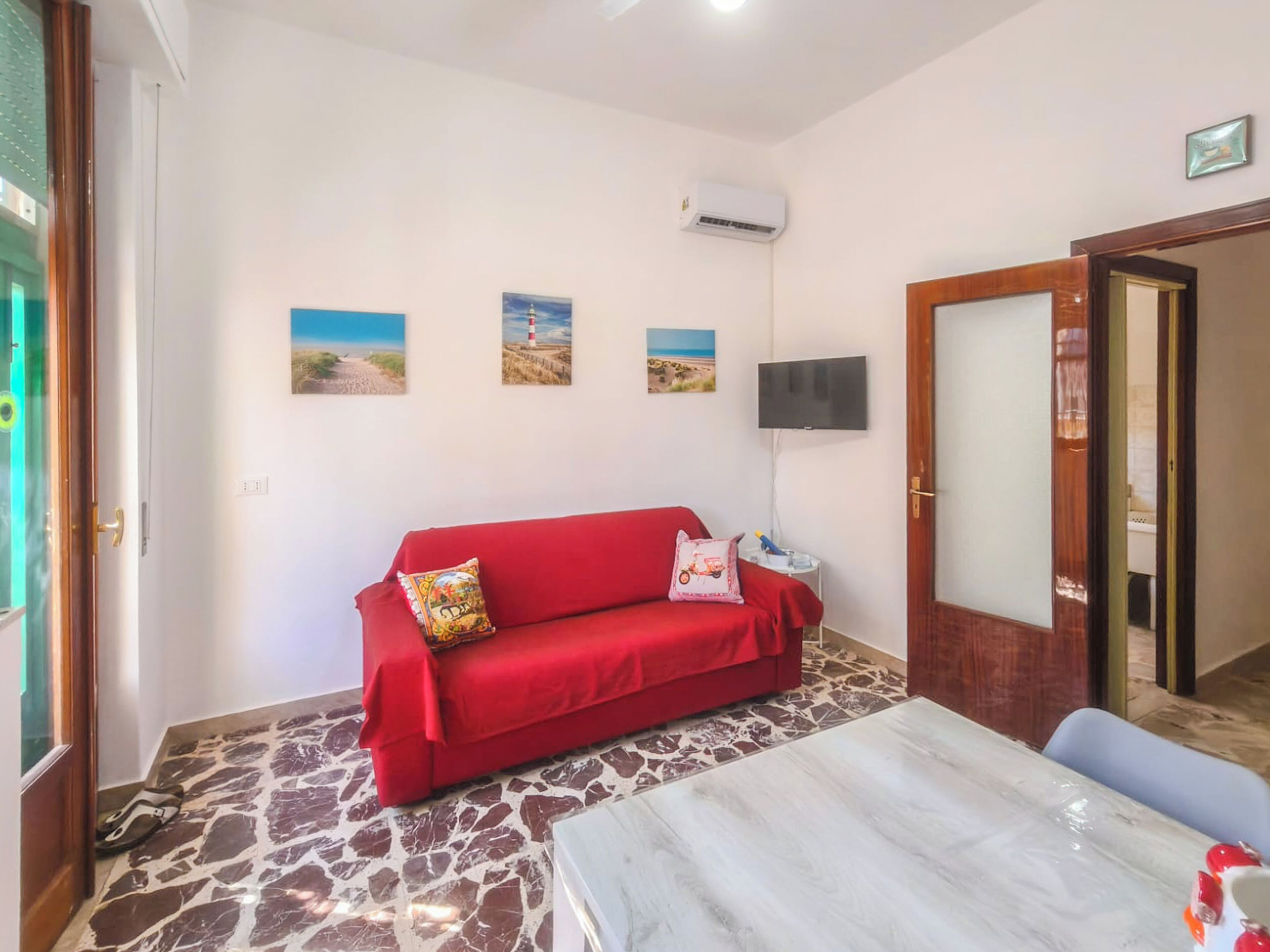 Una habitació amb un sofà vermell, un televisor penjat a la paret i un paviment amb dibuixos.