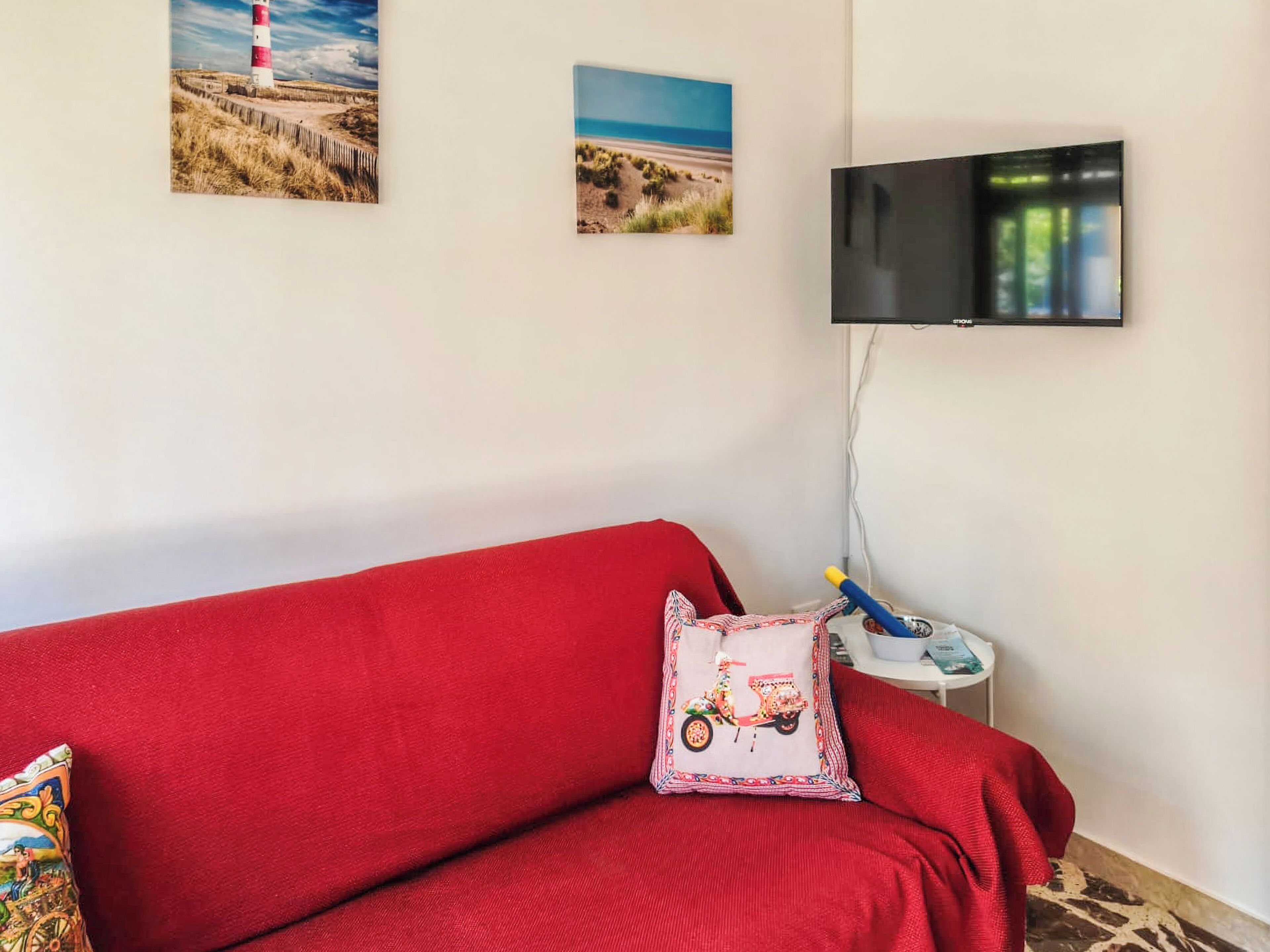 A red sofa with a scooter pillow, a television mounted on the wall, and two framed pictures.