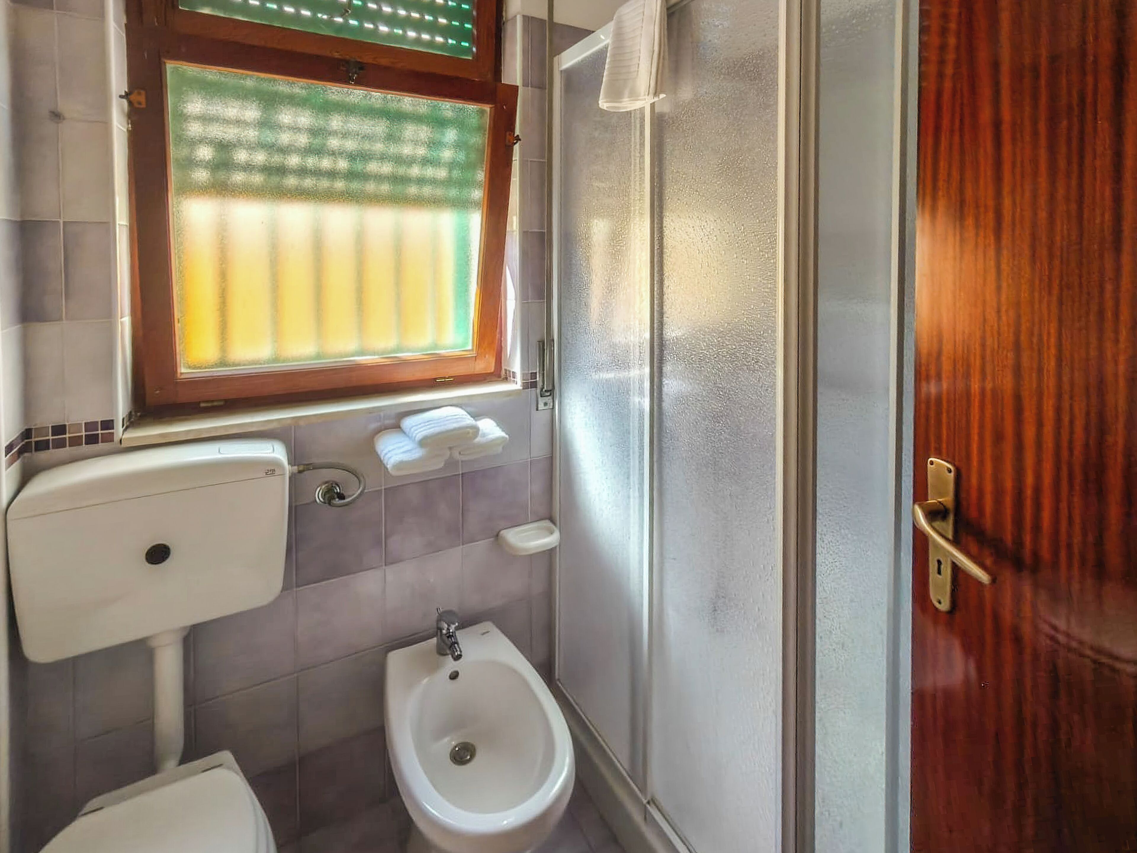Une salle de bain équipée de toilettes, d’un bidet et d’une fenêtre avec stores.