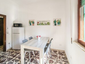 Ein Essbereich mit einem Marmortisch, grauen Stühlen, einem weißen Kühlschrank und Wandkunst mit Kaktusmotiven.
