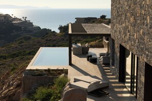 Ein moderner Poolbereich im Freien mit Blick auf das Meer, Steinmauern und Sitzmöglichkeiten.