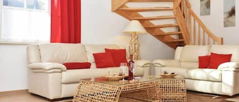 Una sala de estar con dos sofás, una escalera de madera y una mesa de centro de cristal.