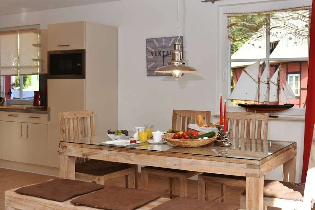 A dining area with a wooden table, chairs, and a glass-top table. There is a window with curtains and a view of a building outside.